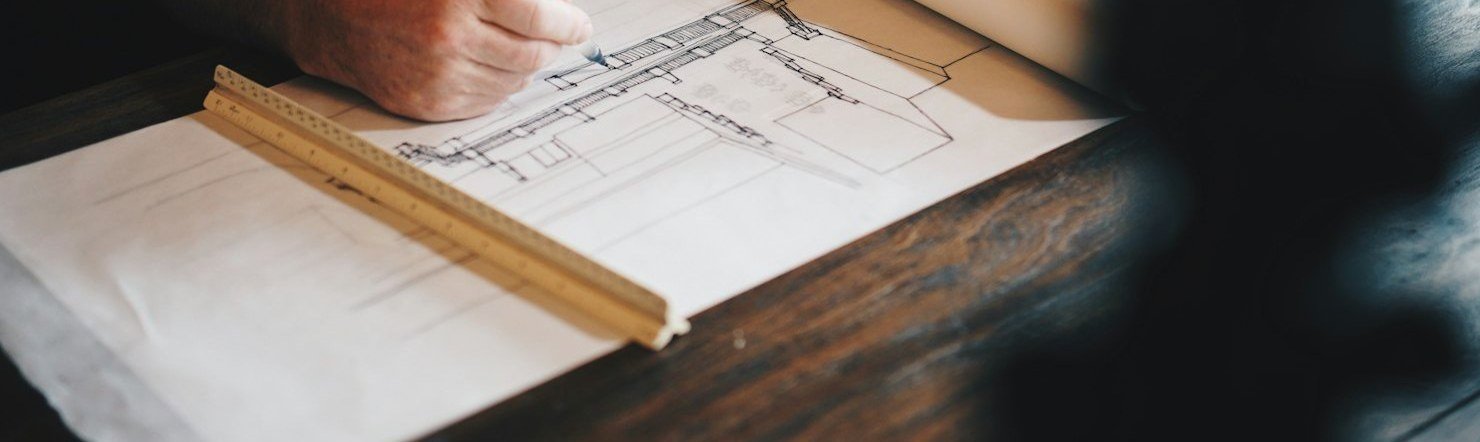Manos dibujando un plano arquitectónico sobre la mesa de trabajo.
