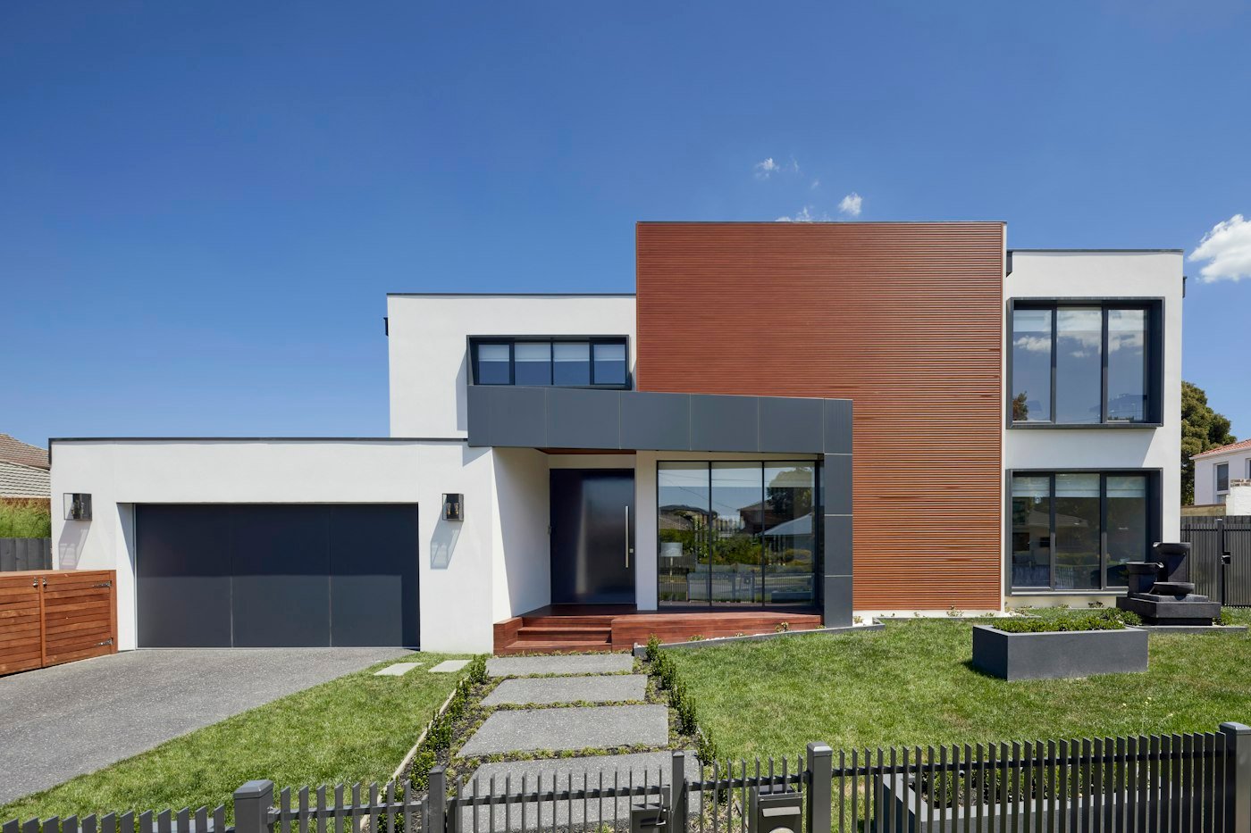 Fachada de casa moderna con duela de madera, cancelería negra y jardín.